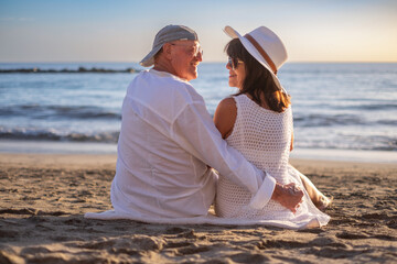 Back view of relaxed senior couple enjoying a sunny day at the beach, smiling while dressed in light summer clothes, conveying love, happiness, and companionship