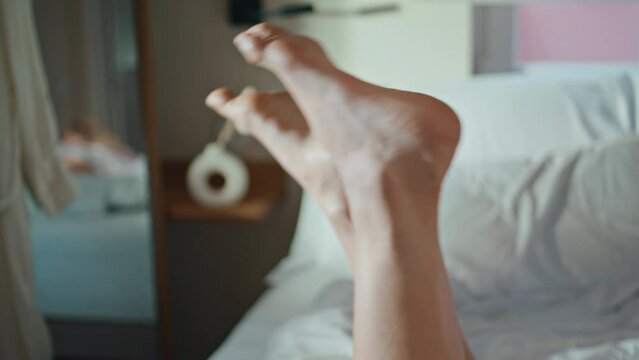 Closeup woman legs bed in morning sunlight. Carefree happy girl dangling feet