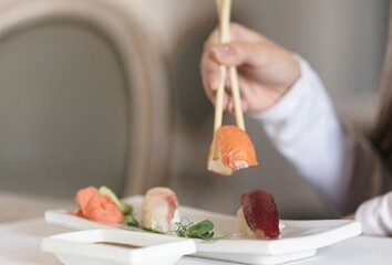 A close-up shot of a hand using chopsticks to pick up a piece of salmon nigiri from a plate of sushi in a modern restaurant setting