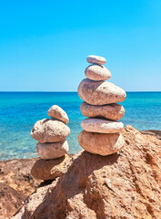Balanced Stacked Stones on Rocky Shore with Clear Blue Sea Background