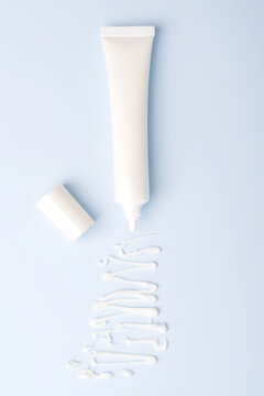 White squize tube with light eye cream and sample texture on blue background. Cosmetic texture presentation