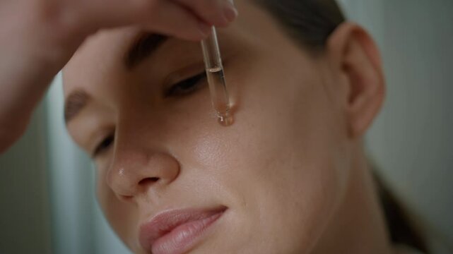 Woman dropping skincare liquid on face closeup. Girl applying nourishing serum