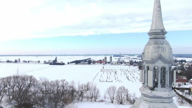 Aerial view of drone passing backwards near the bell tower of the church of St-Benoit de Mirabel in winter, showing the cemetery