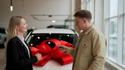 Side view of happy man buyer getting car key and greetings from friendly female auto dealer while buying new auto in dealership. Handsome smiling car owner during handing over keys at auto showroom.
