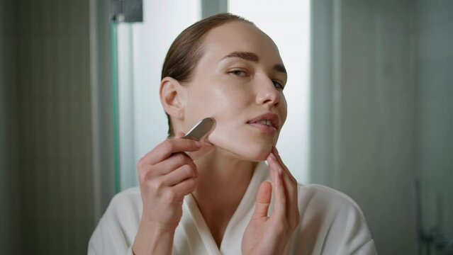 Pretty girl doing gua sha massage closeup. Young woman rolling face in bathroom