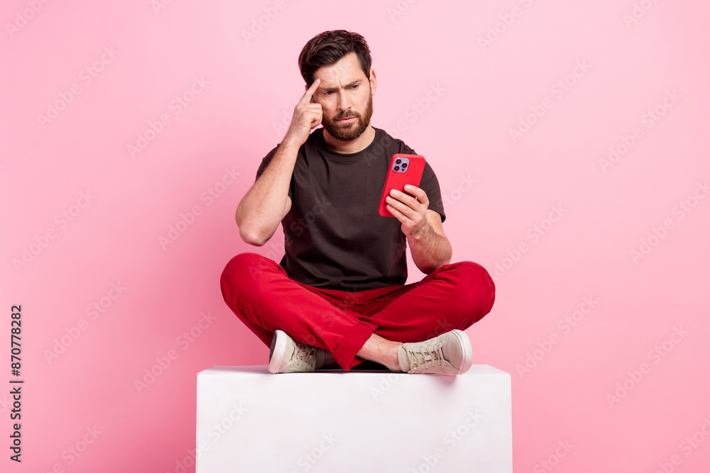 Poster full size photo of smart man dressed brown t-shirt sit on cube look at smartphone finger on forehead