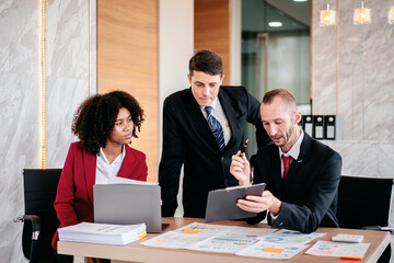 Three men and a woman are sitting at a table with laptops and papers