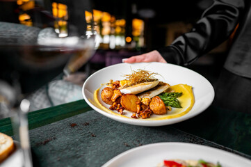 Waiter serving gourmet fish dish with golden garnish in an upscale restaurant.