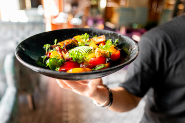 A vibrant salad with fresh greens, tomatoes, and grilled vegetables served on a dark plate.