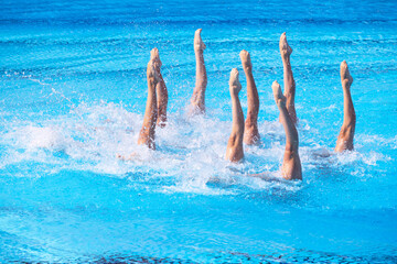 Artistic swimming team performing synchronized legs choreographed movement in swimming pool with copy space