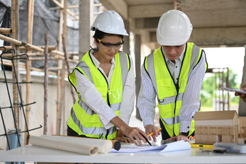 An architect and engineer review blueprints at a construction site. They wear safety gear and work together, pointing out details. Scaffolding and building materials are visible in the background