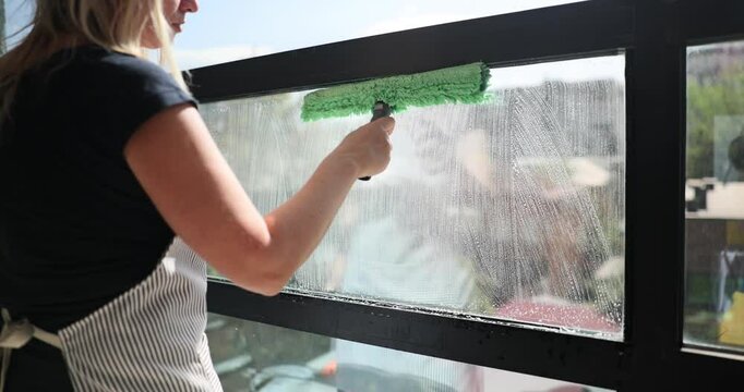 Woman uses brush to wash windowpane with soapy water