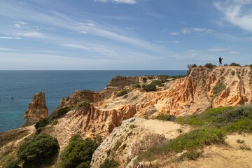 Scenic view of a sandy beach with rocky cliffs and clear blue water in Algarve, Portugal