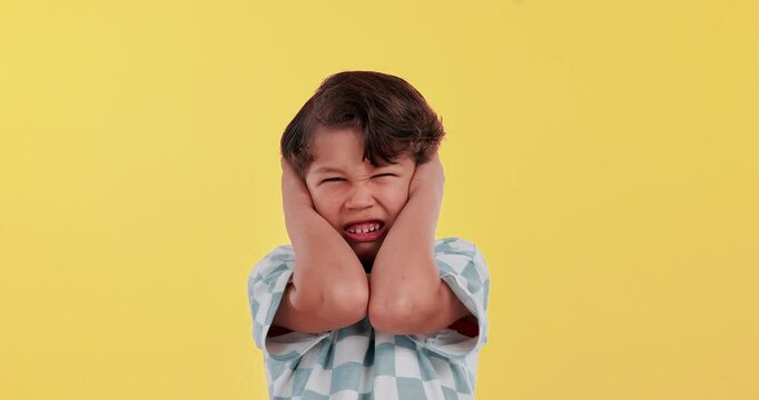 Boy, child and cover ears in studio with frustrated face for noise, anxiety and fear by yellow background. Kid, hands and block for hearing, sound and upset with stress, autism and mental health