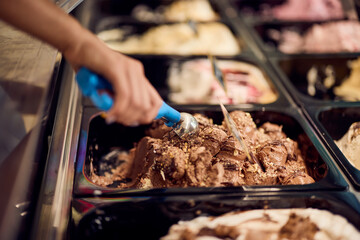 Close-up of the delicious chocolate ice cream in a container, covered in a chocolate syrupy, using a scoop of it.