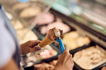 Female worker putting a scoop of ice cream on a cone.