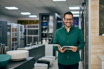 Portrait of a smiling male seller, working at the furniture and sanitary shop, holding one magazine.