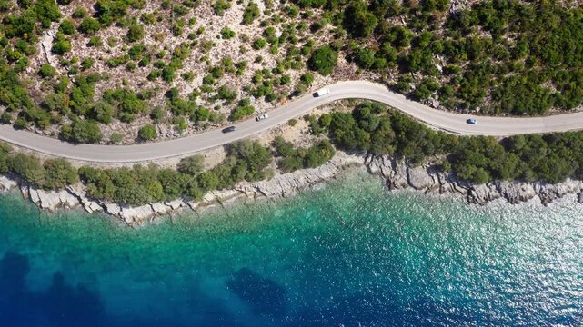 4K Drone footage of casr moving by the sea curved road near a tranquille waves on the Greek coast on Cephalonia island. Transportation, nature concept.