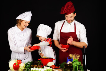 Family preparing tasty food in kitchen. Parents teaching little son to cook healthy meal. Mother, father and cute boy cooking together at home. Happy family in in chef uniform preparing homemade food.