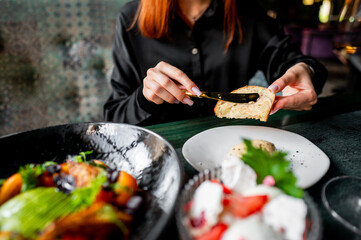 Close-up of hands spreading butter on bread with a knife, with a blurred plate of food in the background