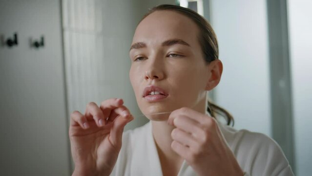 Closeup girl flossing teeth in mirror reflection. Beautiful lady doing dental