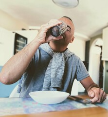 Portrait of young adult man sitting at table, at home drinking.Boy drinking sitting at table.Man alone, sitting at home drinking.Male drinking alone sitting at table.