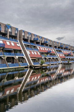 A picturesque scene showing a row of distinctive waterfront homes, their reflections perfectly mirrored in the calm waters of the canal under a cloudy sky in Rotterdam