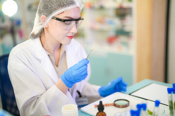 female scientist Experimenting through tubes of chemical liquids and plant samples. In a laboratory with test samples in the background in a modern laboratory By testing safely and cleanly.