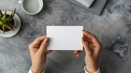 Obraz premium Woman holding blank card at grey table, top view
