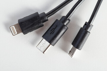 Universal black 3 in 1 charging cable with different charging connectors on a white background, close-up. Type-c, usb-c, micro-usb