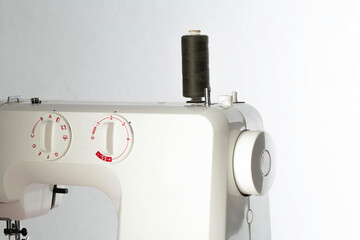 Part of a sewing machine with a black spool of thread against a white wall. Tailoring service concept. Copy space for text, automatical