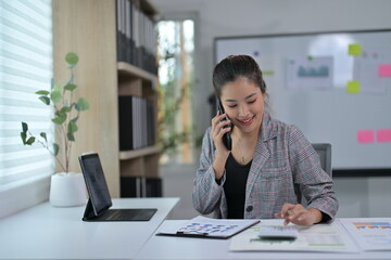 Young Professional Woman Working in Modern Office on Phone Call with Documents and Tablet
