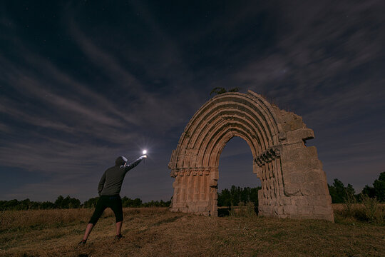 Night view of the arch of the missing church of San Miguel de Mazarreros, in Sasam&oacute;n, Burgos, illuminated by the light of the moon and a man with a light in his hand
