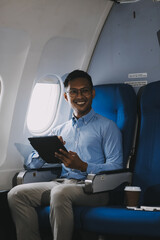 Attractive Asian male passenger of airplane sitting in comfortable seat while working laptop and tablet with mock up area using wireless connection. Travel in style, work with grace.