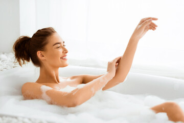 Naklejka premium Happy woman washing body and feel relax in bathtub with foam