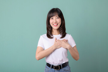 Smiling positive, pretty asian young woman holding heart with hands on light green background.