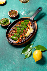 Grilled srimps with lime leaves served on a black iron pot, highlighting vibrant colors and textures against a turquoise background.