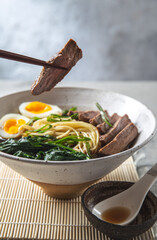 A bowl of ramen with slices of beef, soft-boiled egg halves, and green vegetables. The meal is garnished with green onions