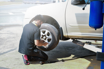 The car attendant  is turning the car wheel back into the car's hub after the tire leak has been repaired, soft and selective focus on wheel, in motion.