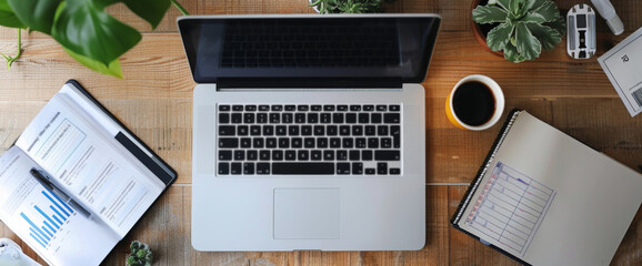 Top view of a office desk with a laptop, charts, plants, and coffee, creating a productive and natural workspace.