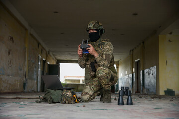 Military mission. Soldier in uniform with drone controller, laptop and binoculars inside abandoned building