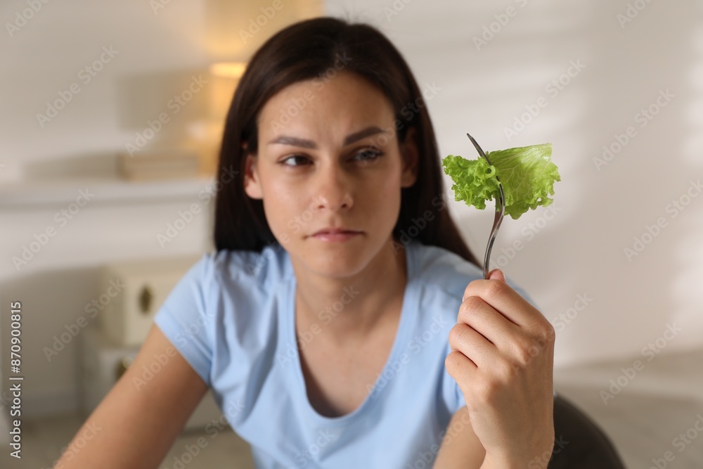 Poster Eating disorder. Sad woman holding fork with lettuce indoors