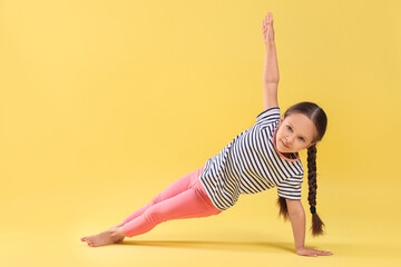 Cute little girl doing gymnastic exercise on yellow background, space for text