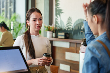 young Asian woman is standing in front of the beverage counter in a cafe. to order coffee With a...