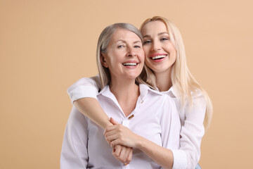 Family portrait of young woman and her mother on beige background