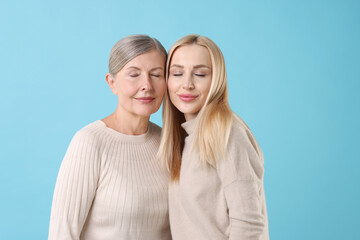 Family portrait of young woman and her mother on light blue background
