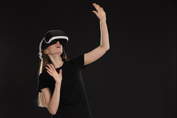 Surprised woman using virtual reality headset on black background, space for text