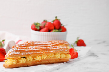Delicious eclairs filled with cream and strawberries on white marble table