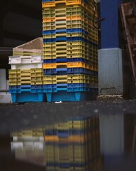 Stack of colorful plastic crates reflected in a puddle in a fisher habor