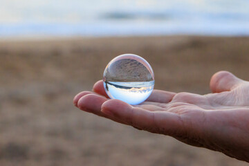 The sunset and the beach and sea of the bay at Agios Georgios on the island of Corfu are reflected in a glass sphere